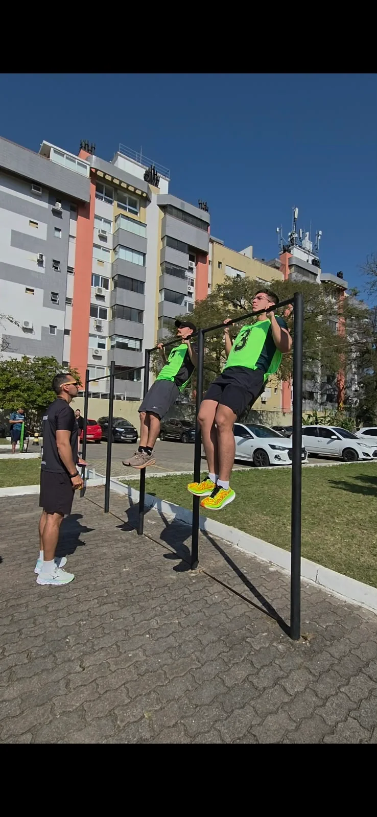 Maicon observando dois participantes realizando exercício na barra.