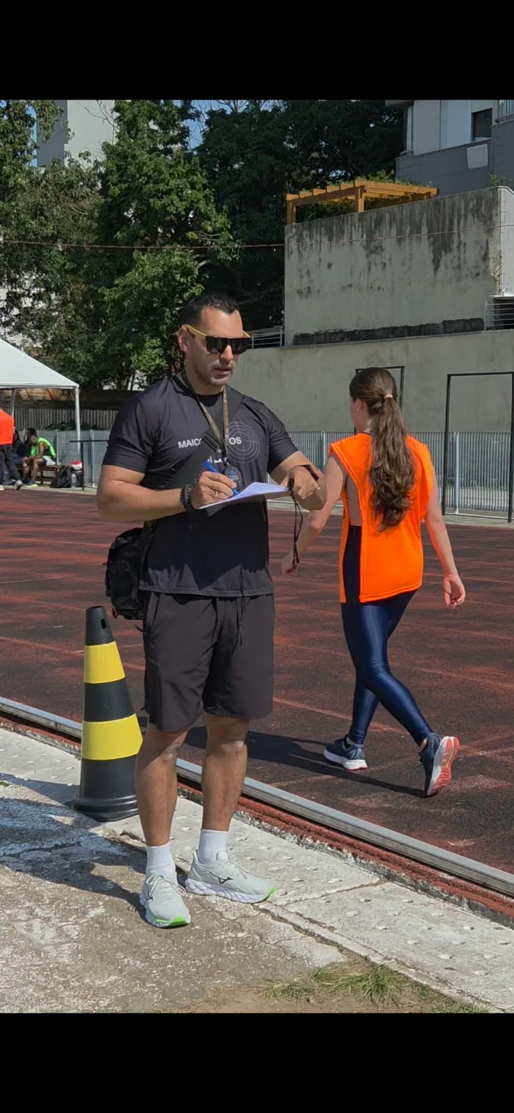 Maicon registrando informações com uma prancheta ao lado de uma pista.