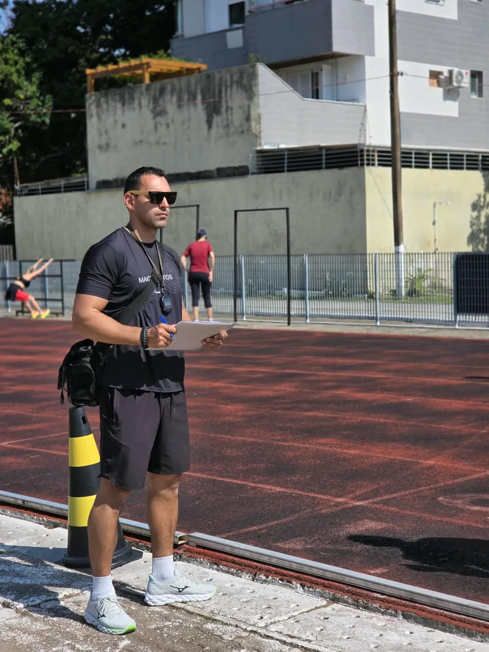 Maicon Santos com prancheta durante uma atividade em pista de atletismo.